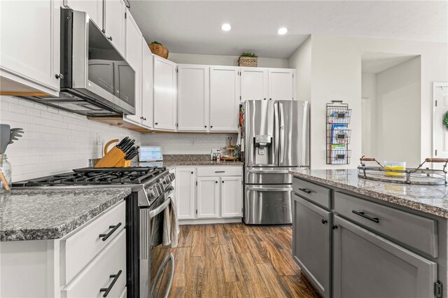 kitchen featuring stainless steel appliances, tasteful backsplash, dark hardwood / wood-style floors, dark stone countertops, and white cabinets