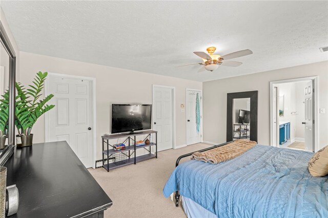 carpeted bedroom featuring a textured ceiling, ensuite bath, and ceiling fan