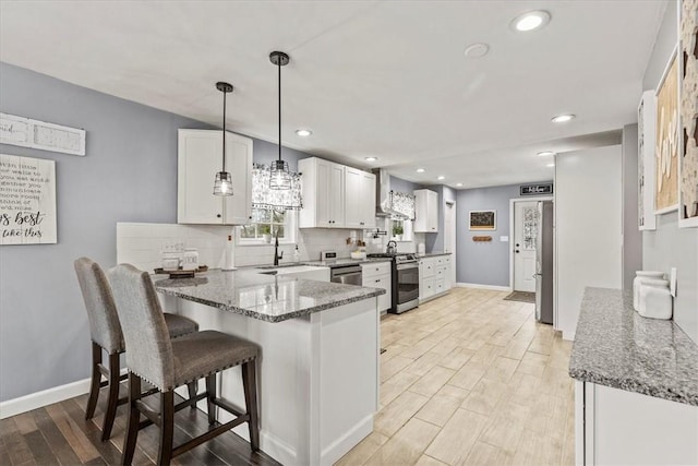 kitchen with wall chimney exhaust hood, stainless steel appliances, kitchen peninsula, pendant lighting, and white cabinets