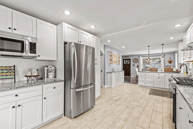 kitchen with appliances with stainless steel finishes, white cabinetry, and hanging light fixtures