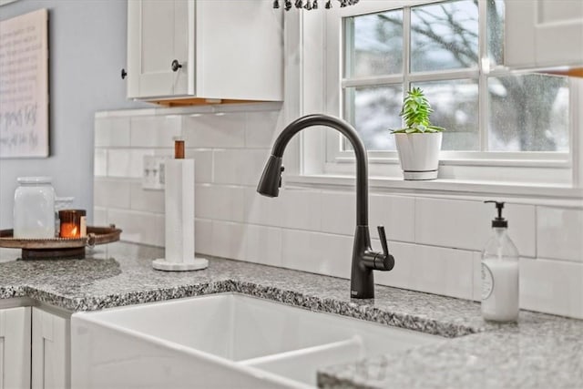 room details featuring tasteful backsplash, light stone countertops, sink, and white cabinets