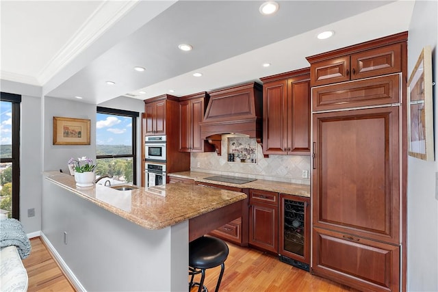 kitchen with custom exhaust hood, light wood-type flooring, wine cooler, backsplash, and a breakfast bar area