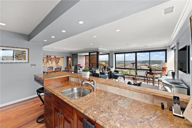 kitchen featuring a breakfast bar area, light hardwood / wood-style floors, crown molding, light stone countertops, and sink