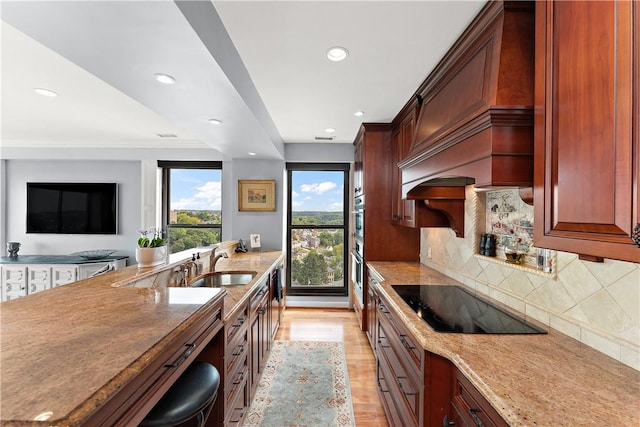 kitchen with light stone counters, light hardwood / wood-style flooring, decorative backsplash, black electric cooktop, and sink