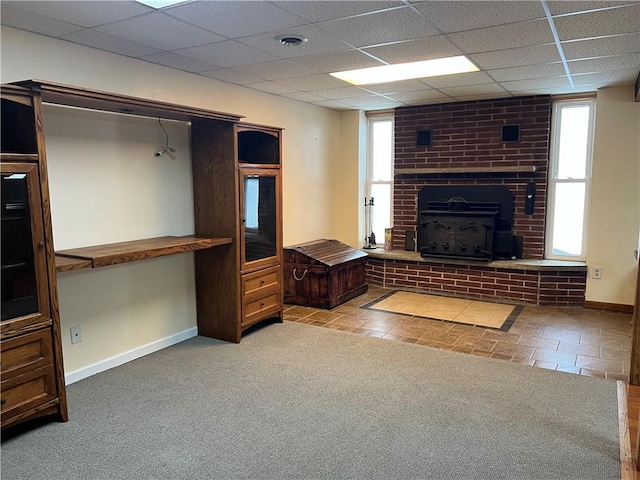 unfurnished living room featuring a wood stove, a healthy amount of sunlight, a paneled ceiling, and light colored carpet