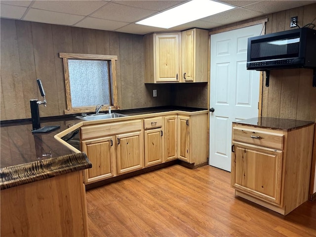 kitchen featuring a drop ceiling, light wood-type flooring, sink, and wooden walls