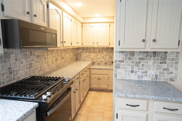 kitchen featuring light tile patterned flooring, decorative backsplash, black appliances, and light stone countertops