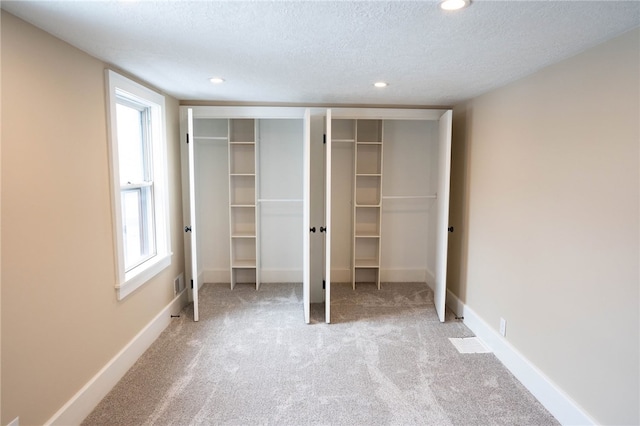 unfurnished bedroom with two closets, baseboards, light colored carpet, recessed lighting, and a textured ceiling