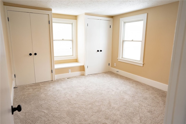 unfurnished bedroom with carpet flooring, baseboards, two closets, and a textured ceiling