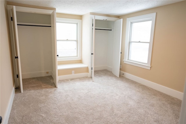 unfurnished bedroom featuring multiple windows, two closets, light carpet, and a textured ceiling