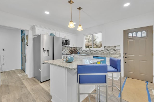 kitchen featuring decorative backsplash, appliances with stainless steel finishes, white cabinets, a kitchen island, and hanging light fixtures