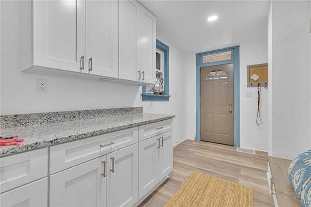 kitchen featuring light stone counters, white cabinets, and light wood-type flooring