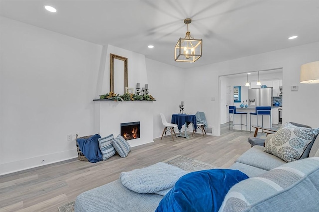 living area with recessed lighting, light wood-style flooring, an inviting chandelier, a lit fireplace, and baseboards