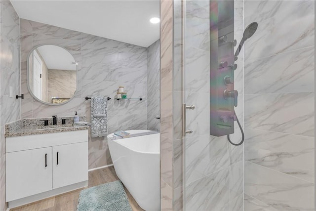 bathroom with wood finished floors, a marble finish shower, vanity, tile walls, and a freestanding bath