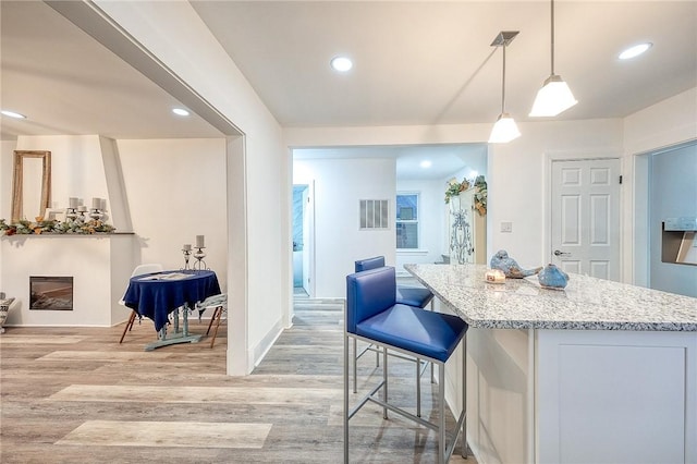 kitchen featuring light stone countertops, open floor plan, a center island, and light wood finished floors