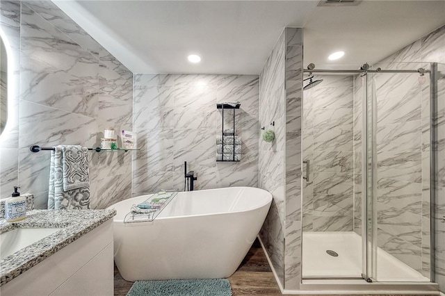full bathroom with tile walls, recessed lighting, wood finished floors, a freestanding tub, and a shower stall