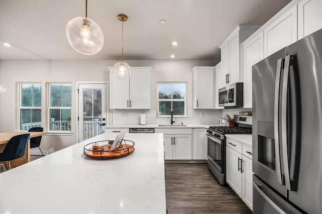 kitchen with white cabinets, stainless steel appliances, decorative backsplash, sink, and hanging light fixtures