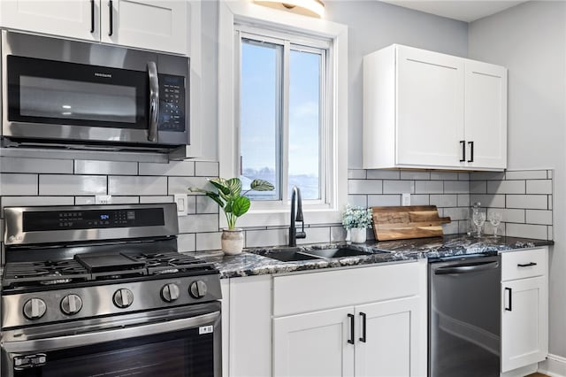 kitchen with appliances with stainless steel finishes, tasteful backsplash, sink, dark stone countertops, and white cabinets