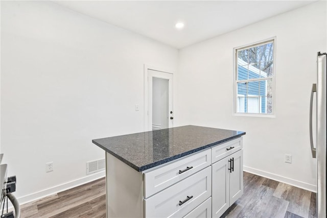 kitchen with dark stone counters, hardwood / wood-style flooring, white cabinets, a kitchen island, and stainless steel refrigerator