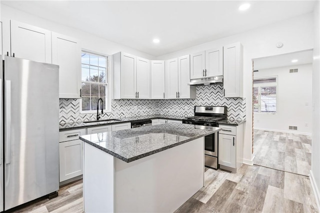 kitchen with white cabinetry, sink, stainless steel appliances, dark stone countertops, and a kitchen island