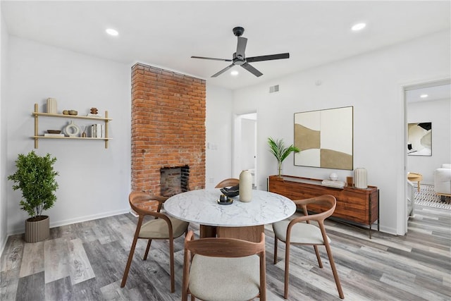 dining area with hardwood / wood-style floors, ceiling fan, and a brick fireplace