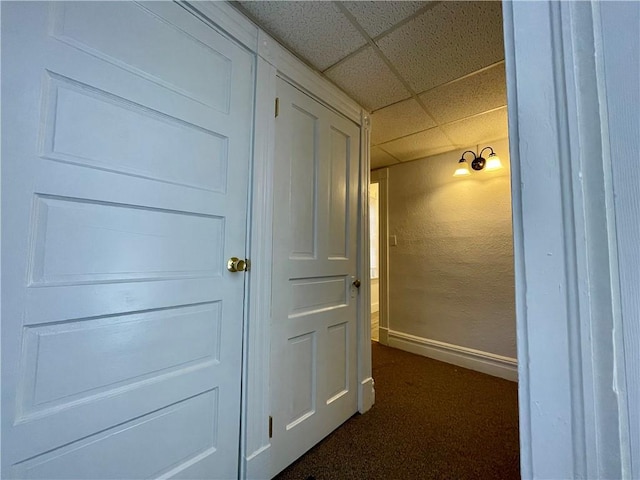 hallway with a paneled ceiling and dark colored carpet