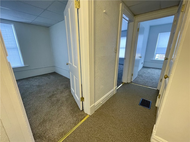 corridor featuring a paneled ceiling and dark carpet