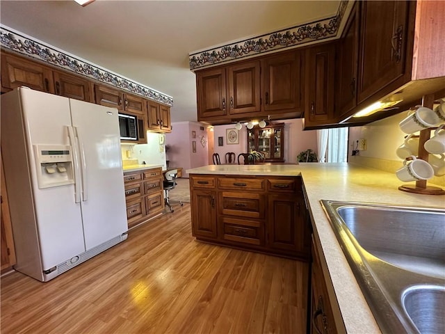 kitchen with sink, light hardwood / wood-style flooring, white fridge with ice dispenser, built in microwave, and kitchen peninsula