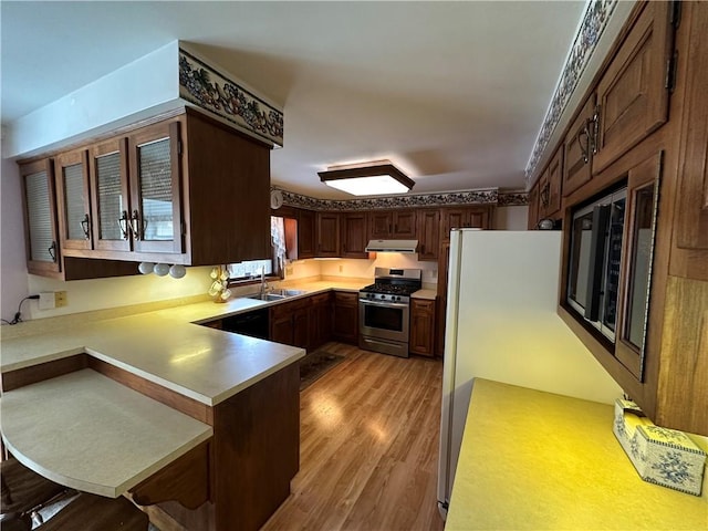 kitchen with gas range, sink, light hardwood / wood-style flooring, kitchen peninsula, and a breakfast bar