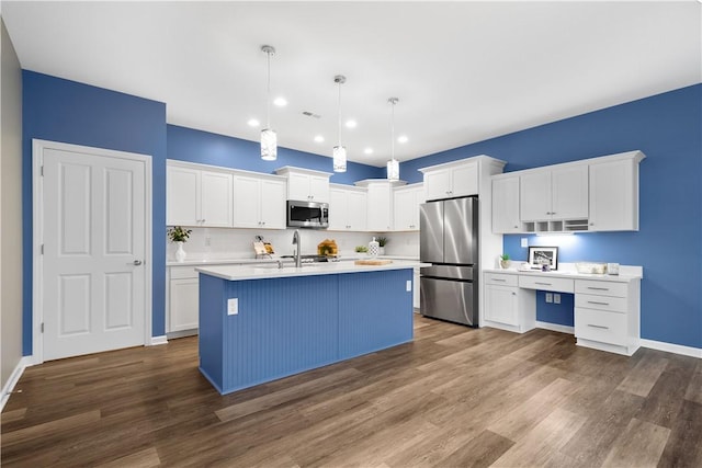 kitchen with hanging light fixtures, a center island with sink, white cabinets, and stainless steel appliances