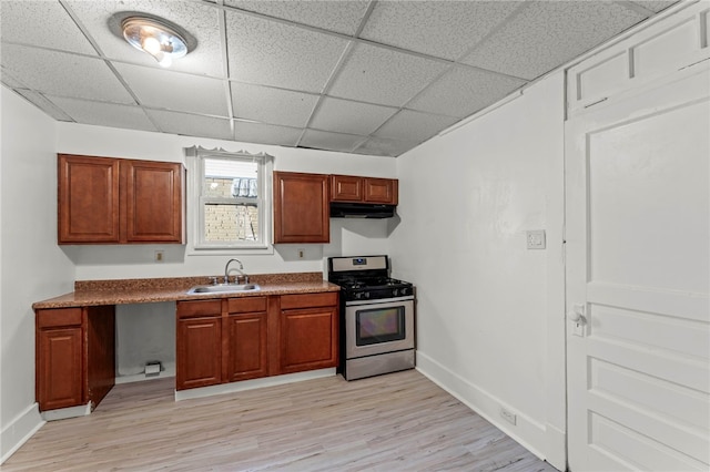 kitchen with a paneled ceiling, stainless steel gas range oven, sink, and light hardwood / wood-style flooring