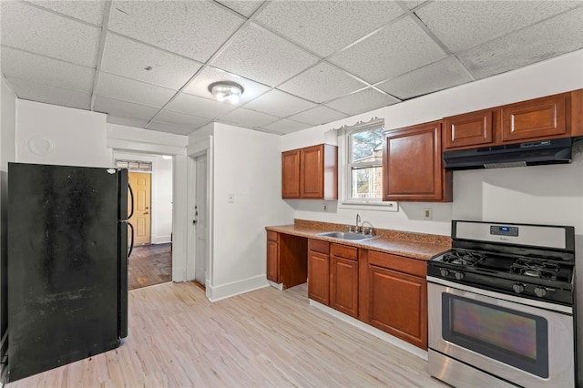 kitchen featuring a paneled ceiling, black refrigerator, sink, light wood-type flooring, and stainless steel range with gas stovetop