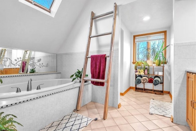 bathroom with tile patterned floors, vaulted ceiling with skylight, and a relaxing tiled tub