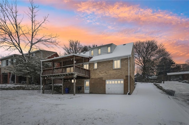 snow covered back of property with a garage and a deck