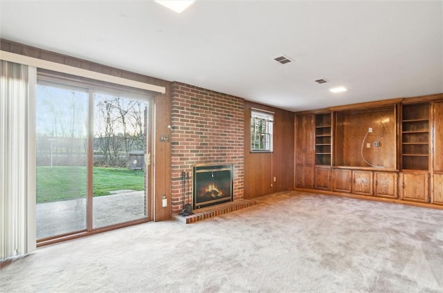 unfurnished living room featuring carpet, wooden walls, and a brick fireplace