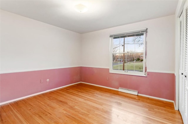 unfurnished bedroom featuring baseboard heating, a closet, and hardwood / wood-style floors