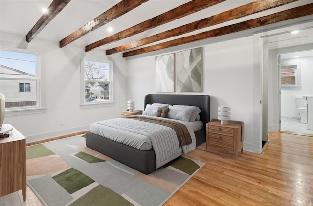 bedroom with beamed ceiling, light wood-type flooring, and ensuite bathroom