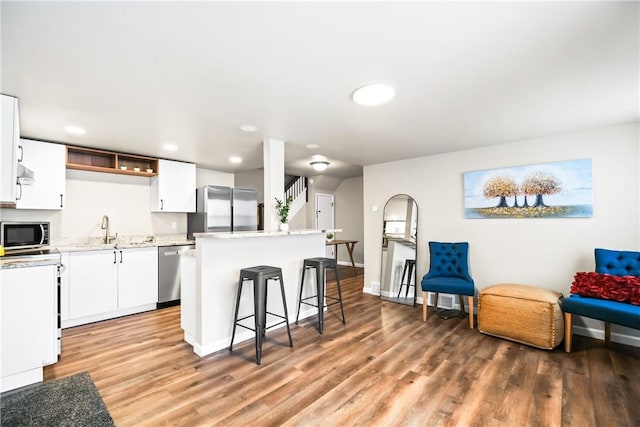 kitchen with stainless steel appliances, sink, wood-type flooring, a center island, and white cabinetry