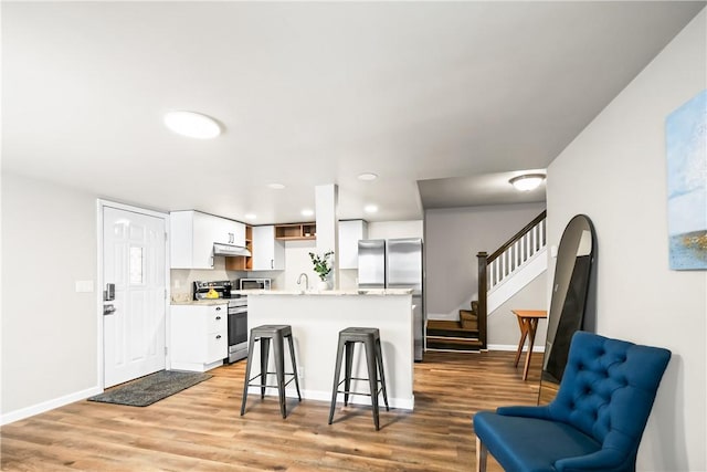 kitchen with white cabinetry, light hardwood / wood-style floors, a breakfast bar, a kitchen island, and appliances with stainless steel finishes