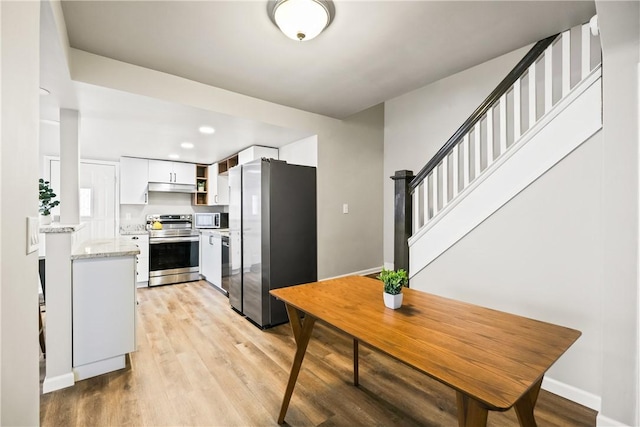 kitchen with light stone countertops, white cabinetry, light hardwood / wood-style flooring, and stainless steel appliances