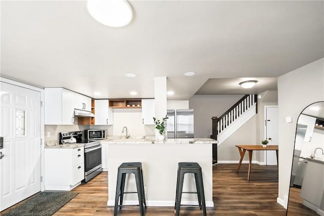 kitchen with sink, appliances with stainless steel finishes, white cabinetry, light stone counters, and wood-type flooring