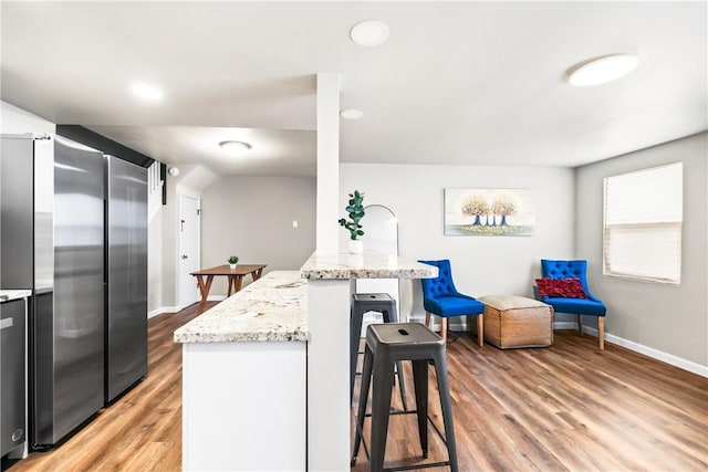 kitchen featuring a breakfast bar area, high end refrigerator, light stone countertops, and hardwood / wood-style flooring