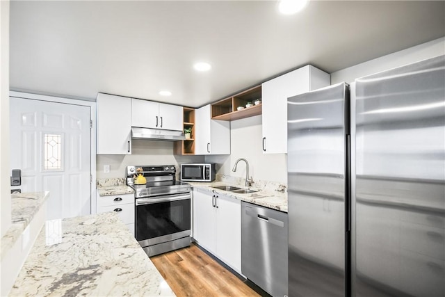 kitchen with sink, light stone counters, appliances with stainless steel finishes, white cabinets, and light wood-type flooring