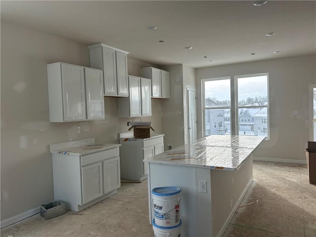 kitchen with white cabinets, a kitchen island, and light stone counters