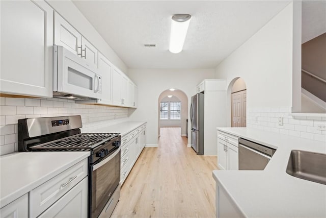 kitchen with sink, stainless steel appliances, tasteful backsplash, light hardwood / wood-style floors, and white cabinets