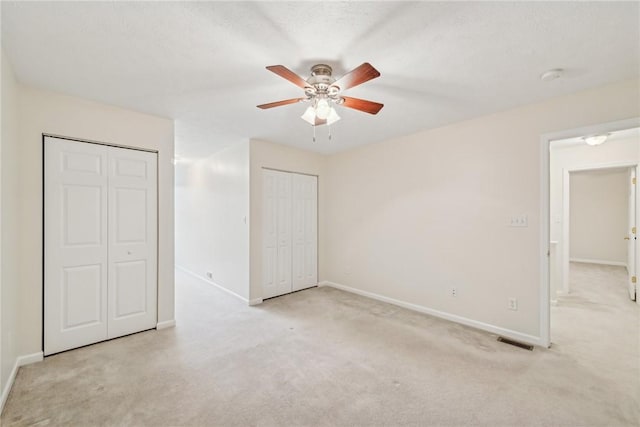 unfurnished bedroom with two closets, light colored carpet, and ceiling fan