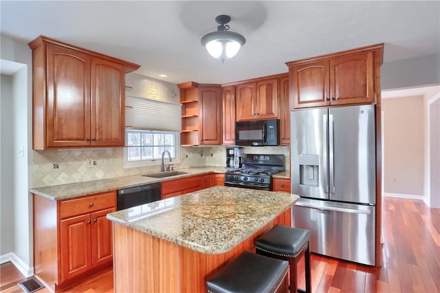 kitchen with sink, a center island, backsplash, wood-type flooring, and black appliances