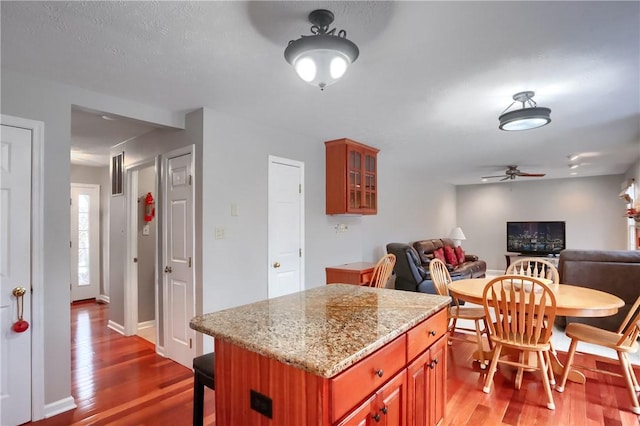 kitchen with light stone countertops, a kitchen bar, ceiling fan, hardwood / wood-style floors, and a kitchen island