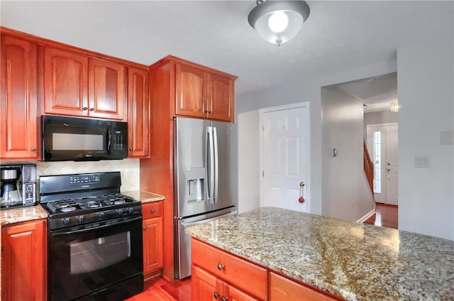 kitchen with decorative backsplash, light stone counters, black appliances, and light wood-type flooring