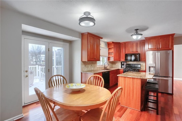 kitchen with light stone countertops, sink, a center island, light hardwood / wood-style flooring, and black appliances